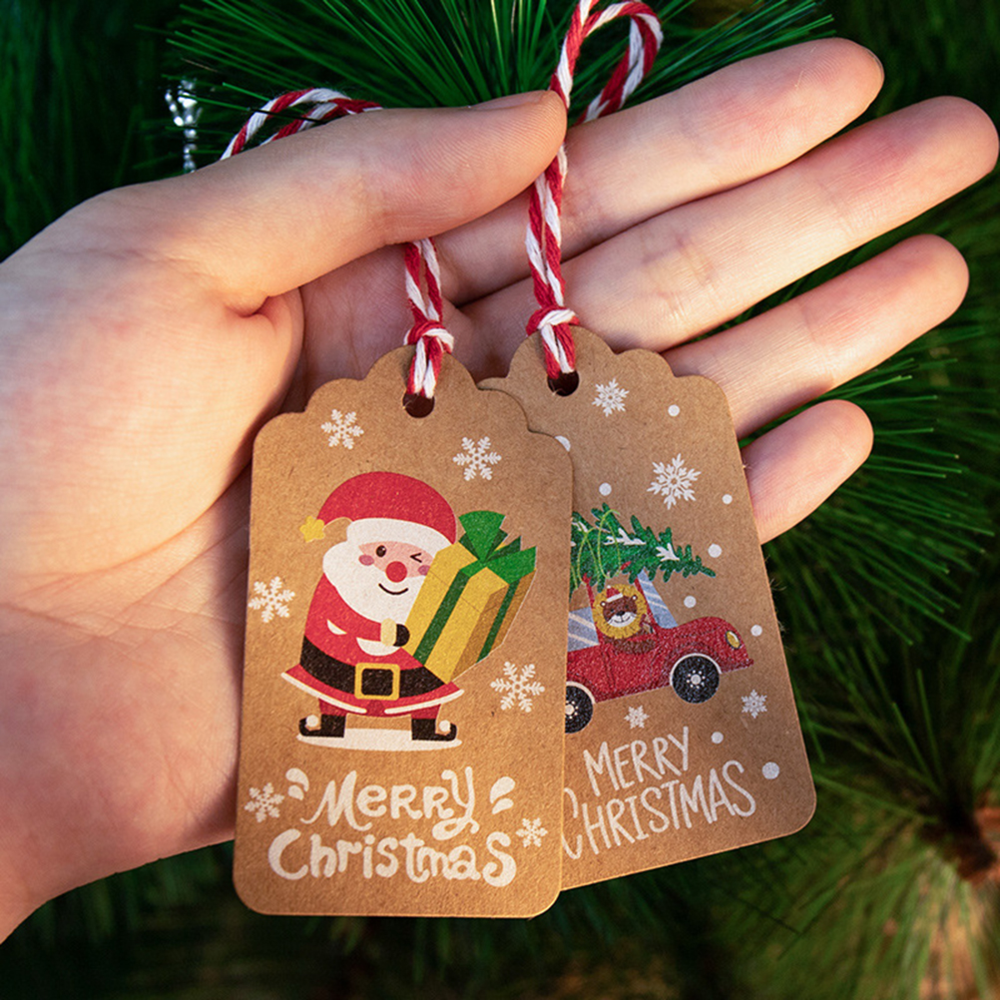 Hand hält zwei braune Weihnachtsetiketten mit Santa und einem Auto.