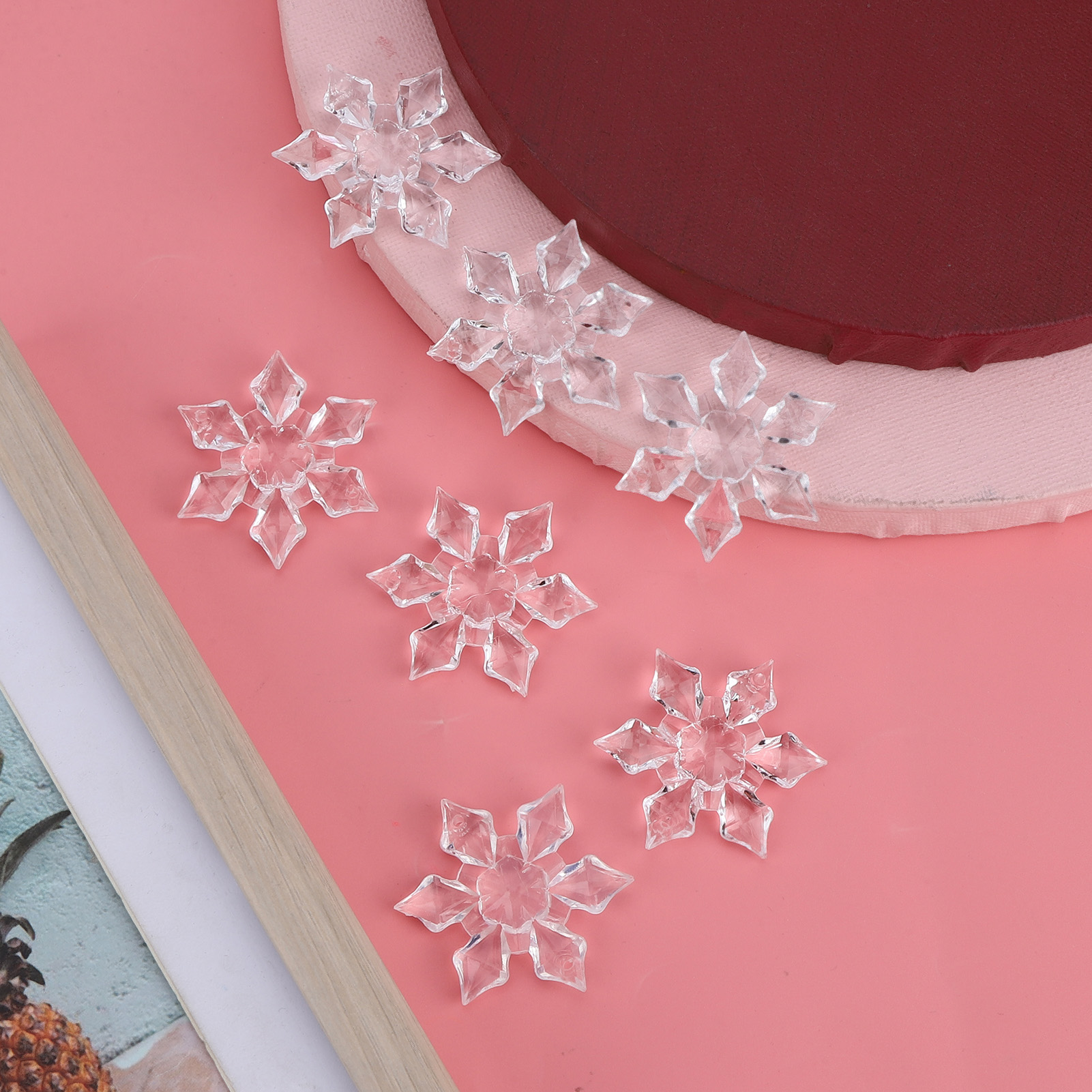 Sechs klare Acryl-Schneeflocken auf rosa und rotem Hintergrund mit Holzrand.