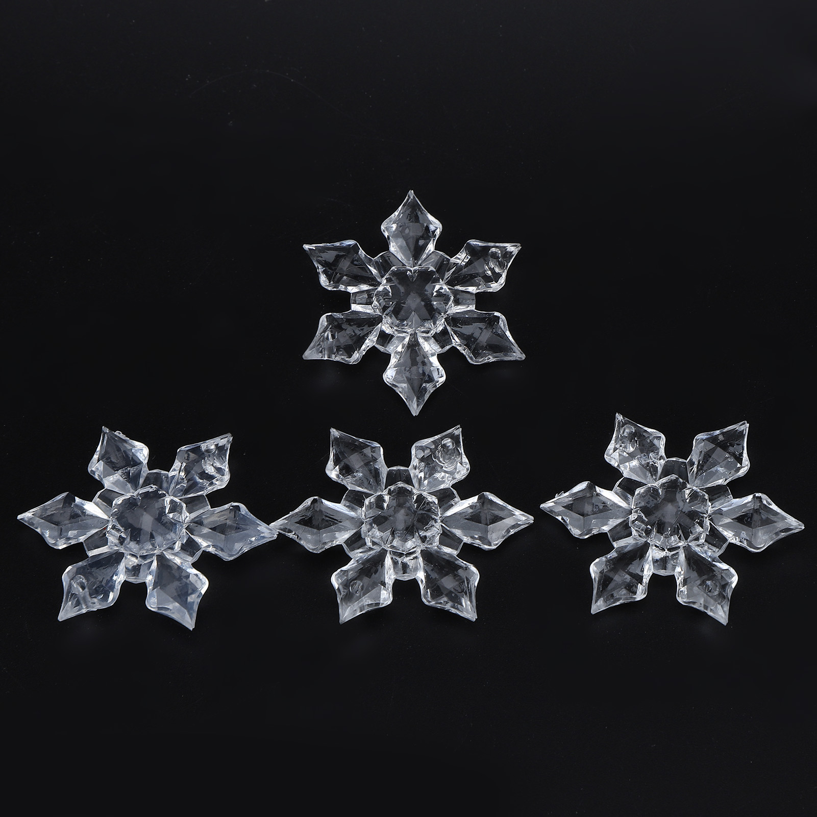 Vier klare, facettierte Acryl-Schneeflocken-Ornamente auf schwarzem Hintergrund.