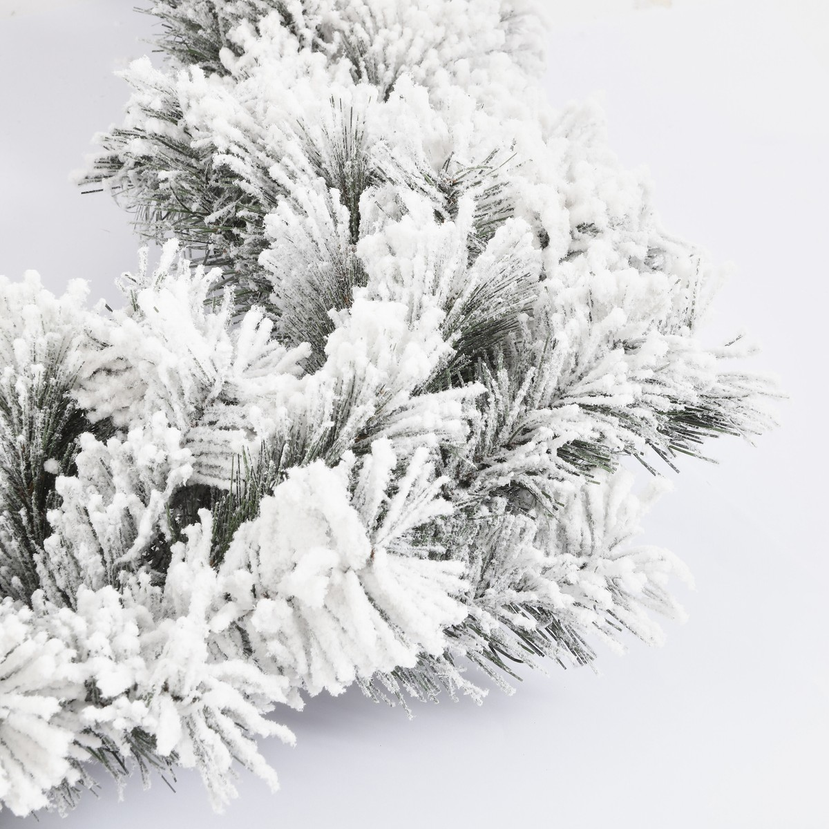 Kunstmatige dennentakken bedekt met dikke, witte nepsneeuw tegen een lichte achtergrond.