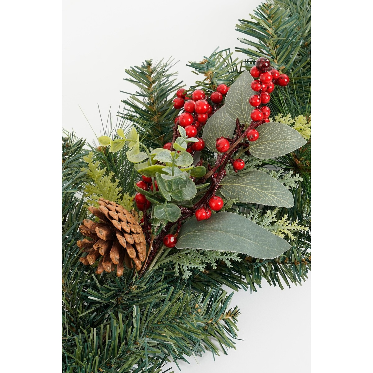 Close-up van een kerstslinger met groene dennennaalden, rode bessen, lichtgroene bladeren en een bruine dennenappel.