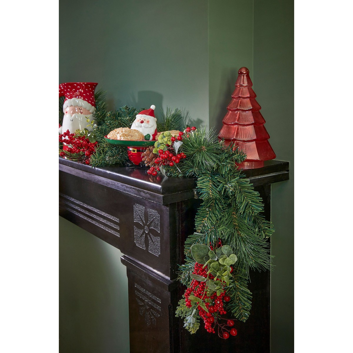 Kerstopenhaarddecoratie met dennenguirlande, rode bessen, kerstmanfiguren en een rode boom.
