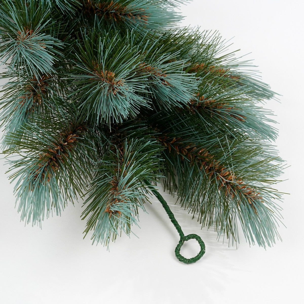 Kunstmatige dennentak met blauwgroene naalden en een draadlus op een witte achtergrond.