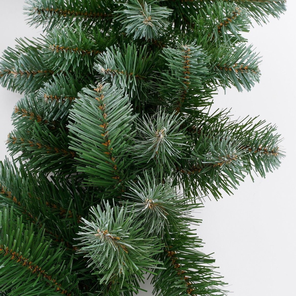 Close-up van een kunstmatige groene denneguirlande tegen een witte achtergrond.