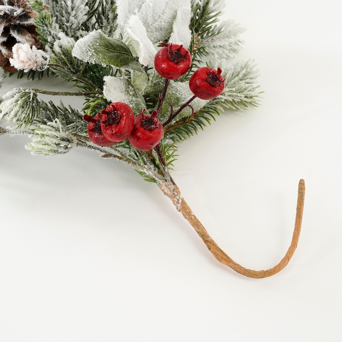 Une branche de pin givrée avec des baies rouges et une pomme de pin sur fond blanc.