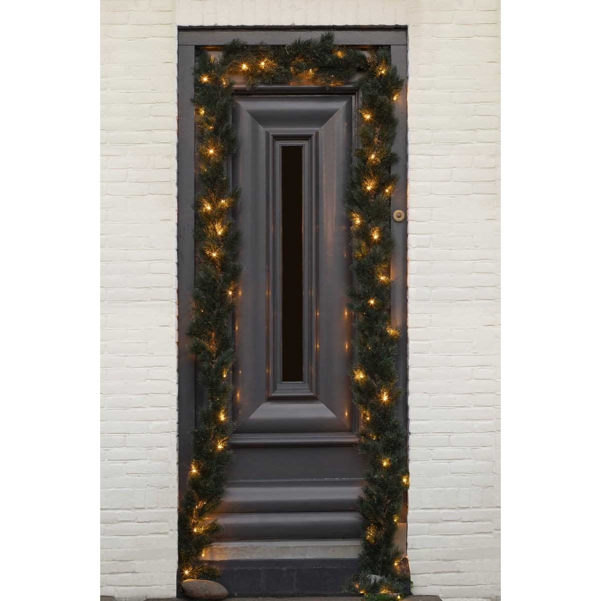 Een grijze voordeur omlijst met een verlichte kerstslinger op witte baksteen.