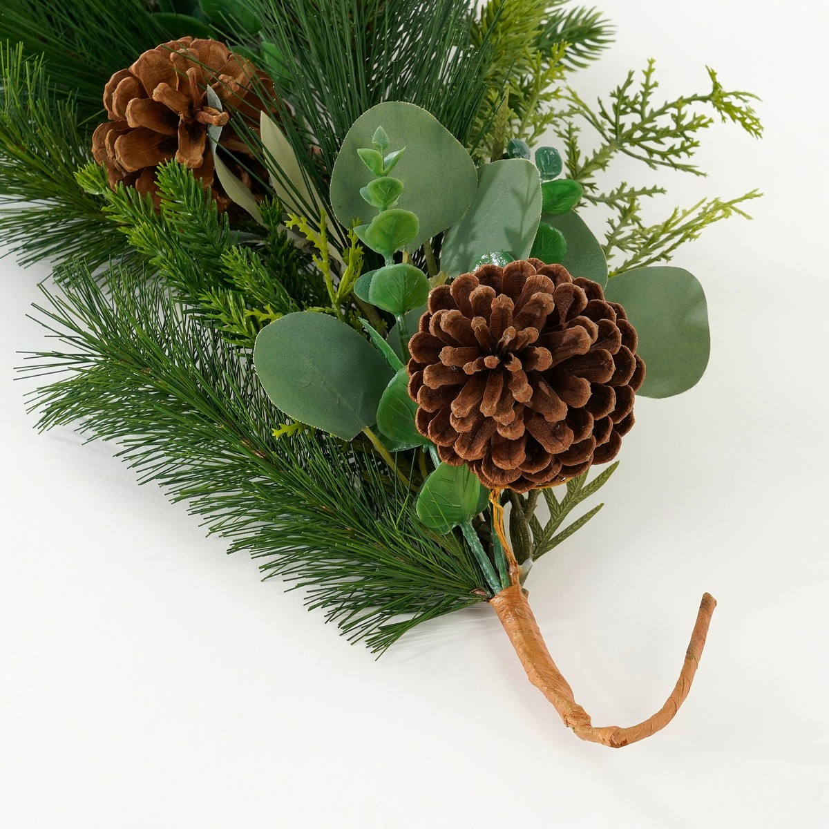 Kunstmatige dennentak met dennenappels en groene bladeren op een witte achtergrond.