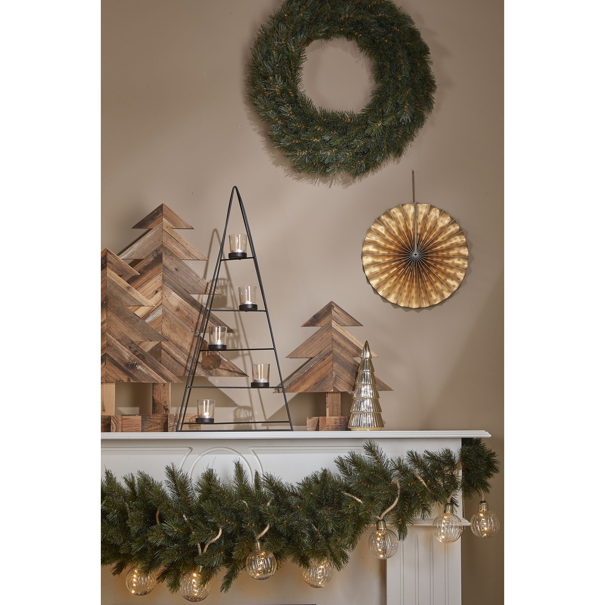 Feestelijke schouw met houten bomen, krans, gouden waaier, piramide kandelaar en lichtsnoer.