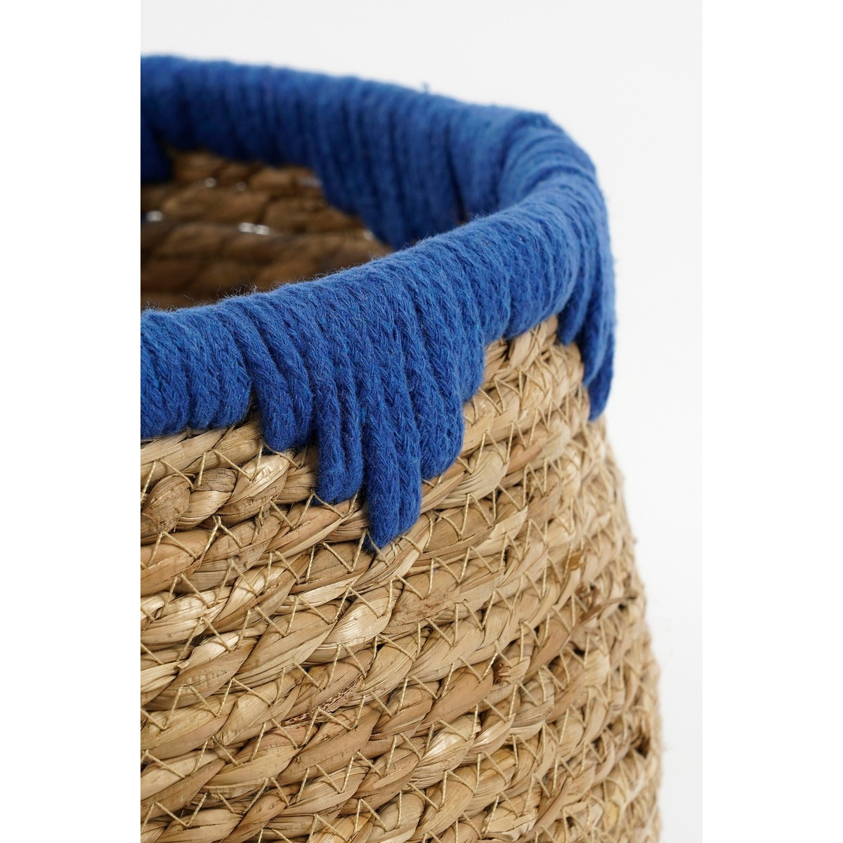 Un panier en jonc de mer tissé avec un tissu bleu épais et texturé autour du bord sur fond blanc.