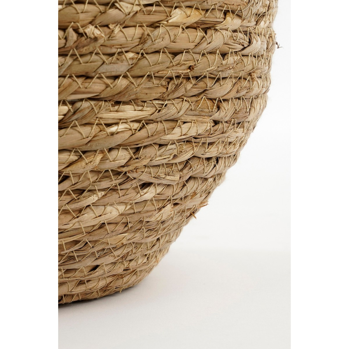 Gros plan sur la texture d'un panier en jonc de mer tissé aux tons beige naturel sur fond blanc.