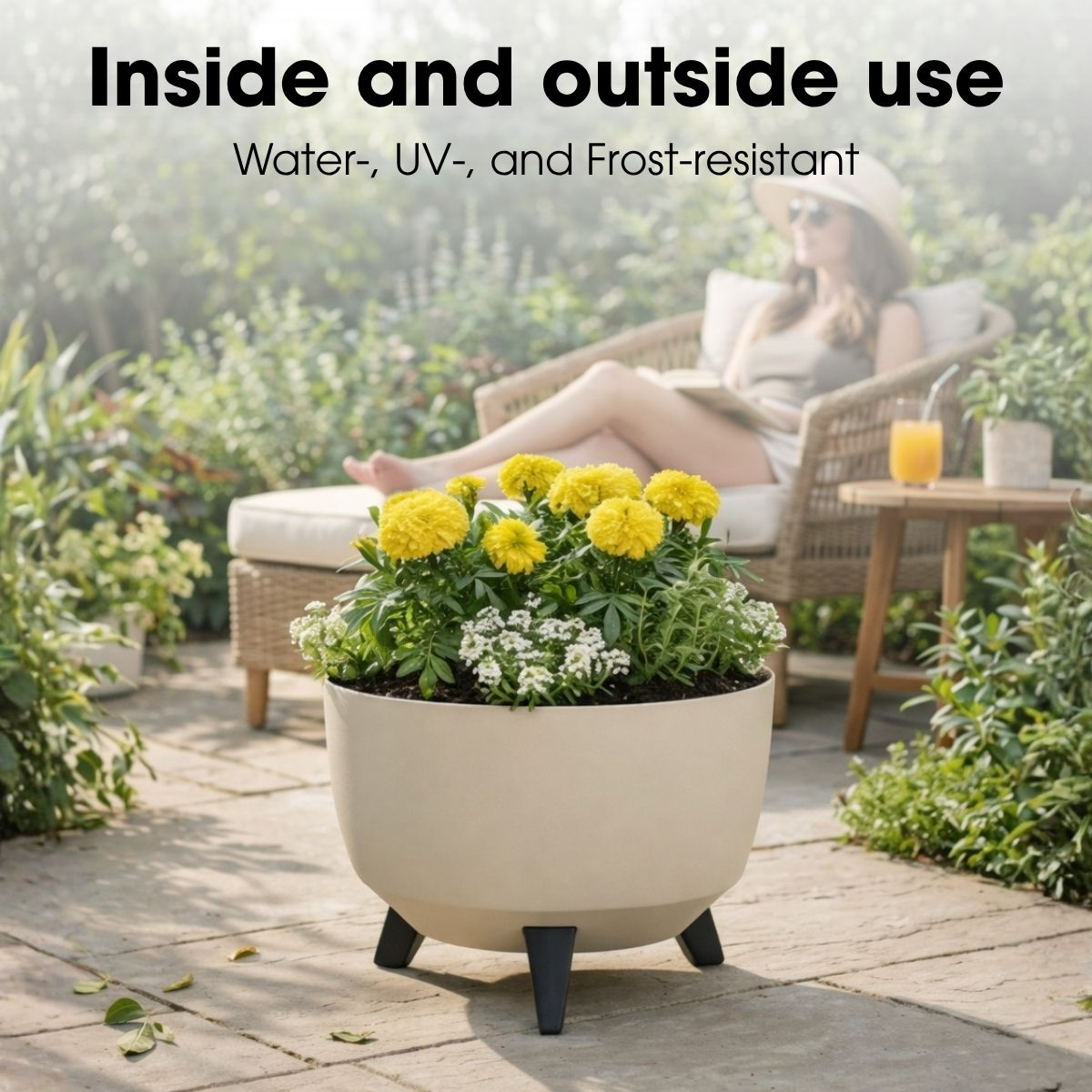 Jardinière ronde beige avec des fleurs jaunes et des pieds noirs, avec une femme se détendant en arrière-plan.
