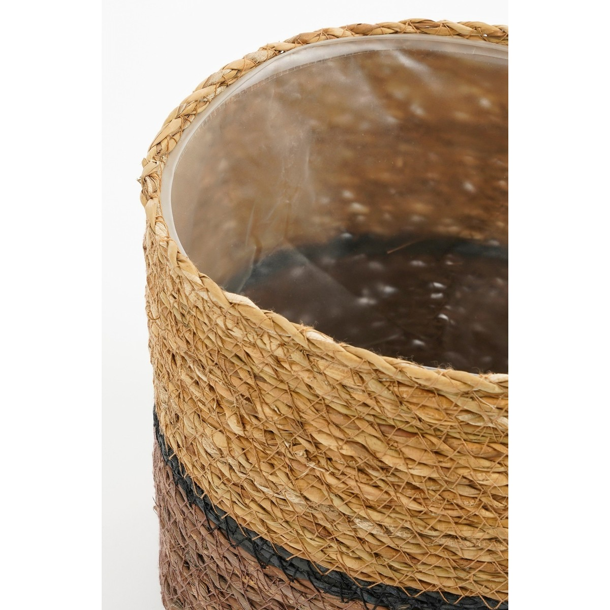 Un panier tressé aux tons naturels, noirs et marrons, avec une doublure en plastique transparent à l'intérieur.