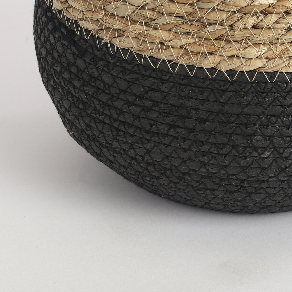 Gros plan d'un panier tressé avec une moitié inférieure noire et une moitié supérieure en paille sur fond blanc.