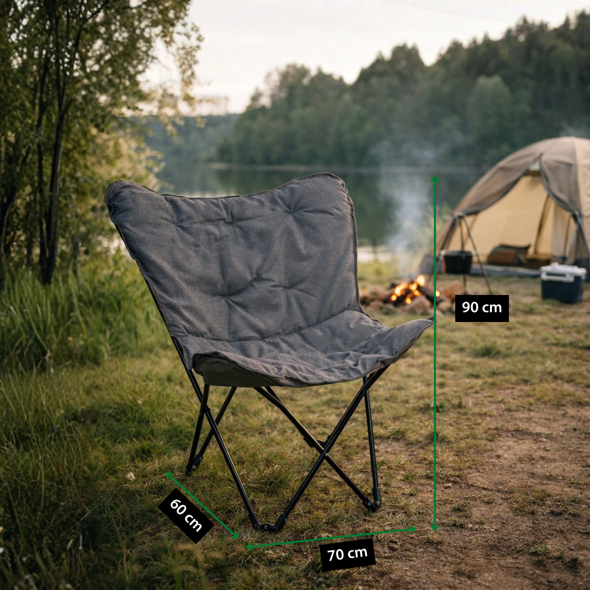 Ein grauer Campingstuhl am See mit Maßen 90 cm Höhe, 70 cm Breite und 60 cm Tiefe. Im Hintergrund ein Zelt und Lagerfeuer.
