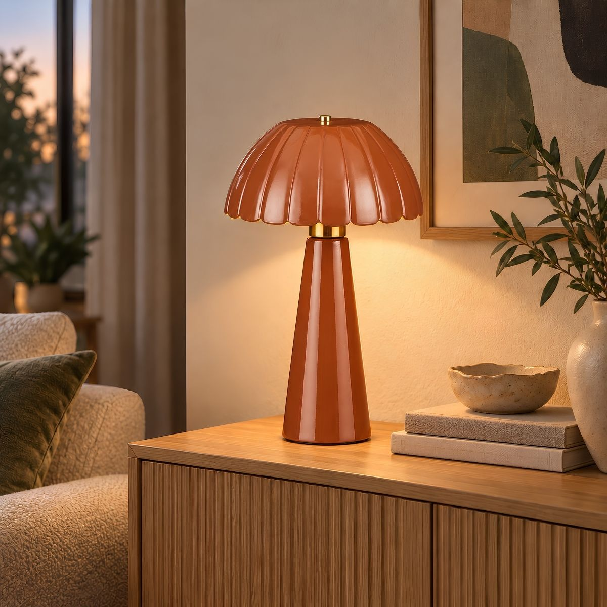 Eine glänzende orange Pilzlampe steht auf einem Holzschrank neben Büchern, einer Schale und Kunst.
