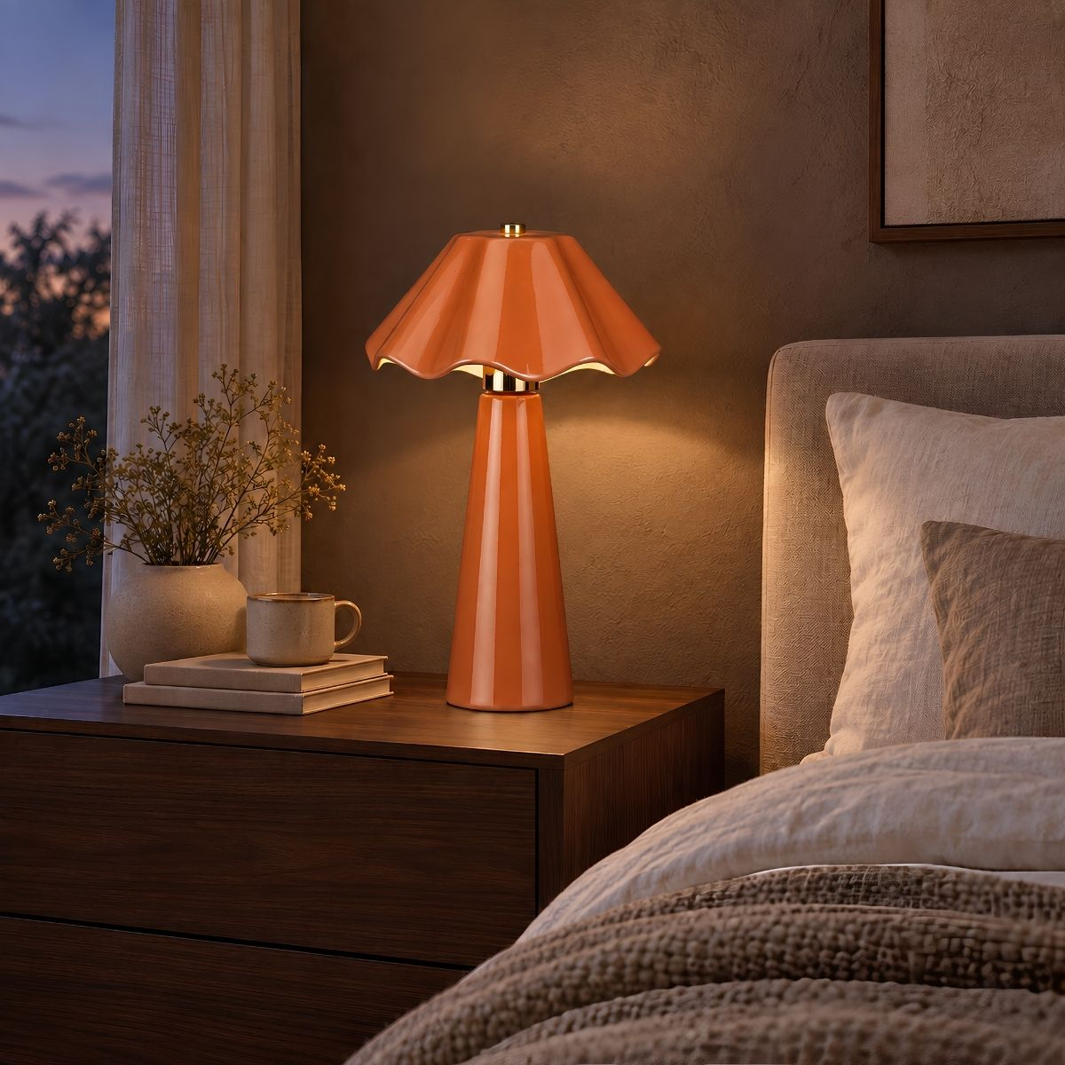 Eine glänzende orange Lampe steht auf einem Nachttisch neben einem Bett, mit einer Vase und Tasse.