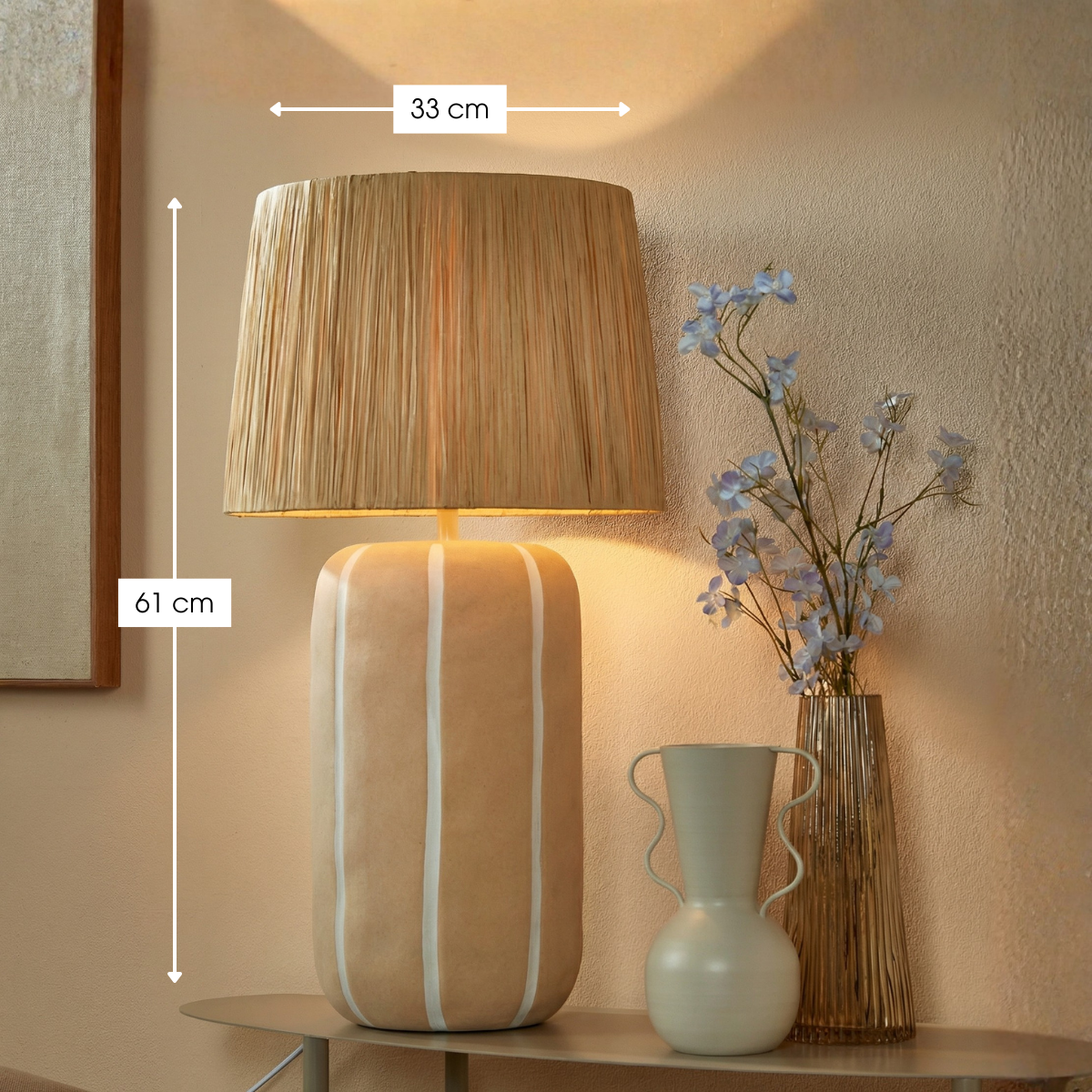 Eine beige Lampe mit Rattan-Schirm und Maßangaben 33 cm und 61 cm steht neben Vasen auf einem Tisch vor beigem Hintergrund.