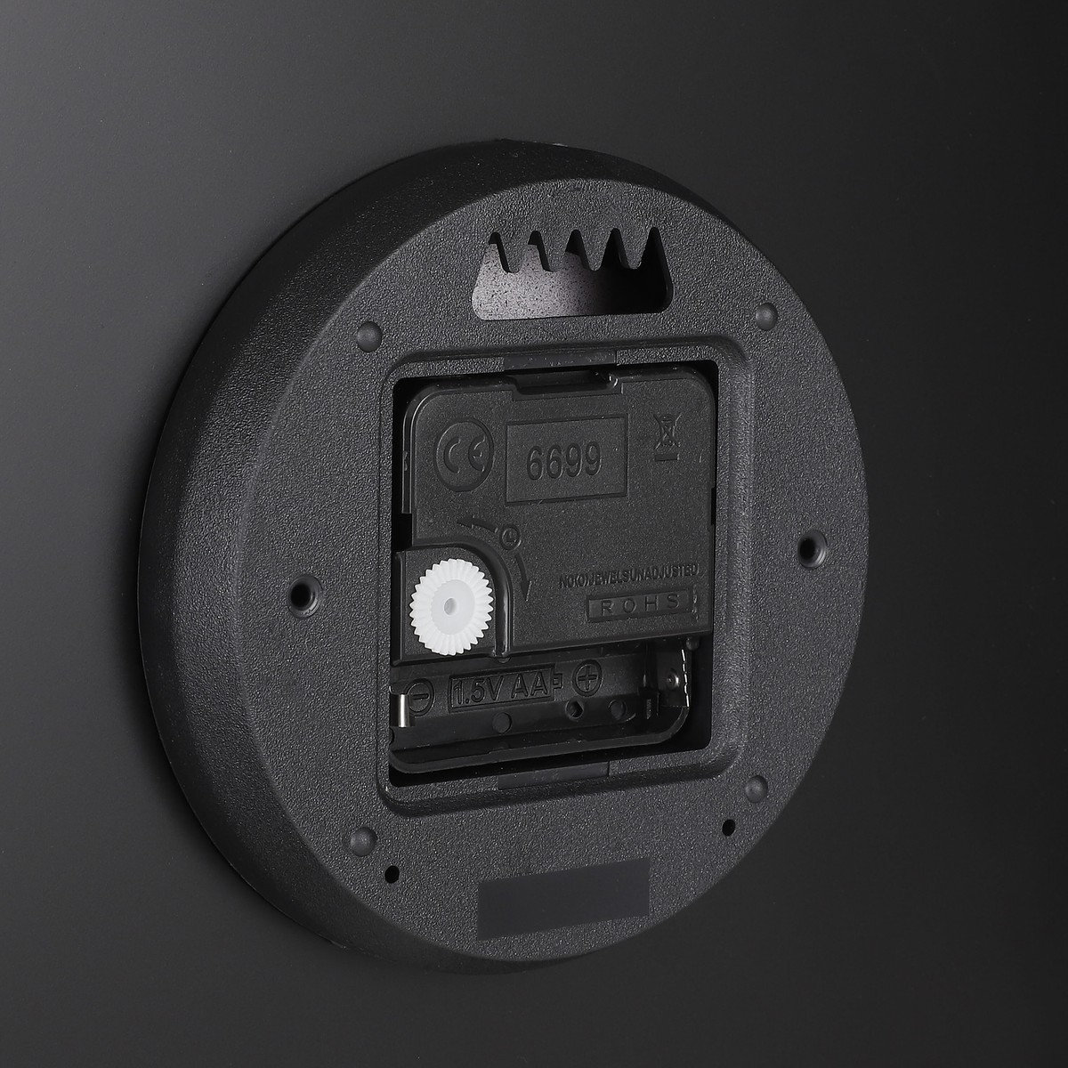 Die Rückseite einer schwarzen Uhr zeigt ein quadratisches Uhrwerk mit einem weißen Zahnrad und einem AA-Batteriefach.