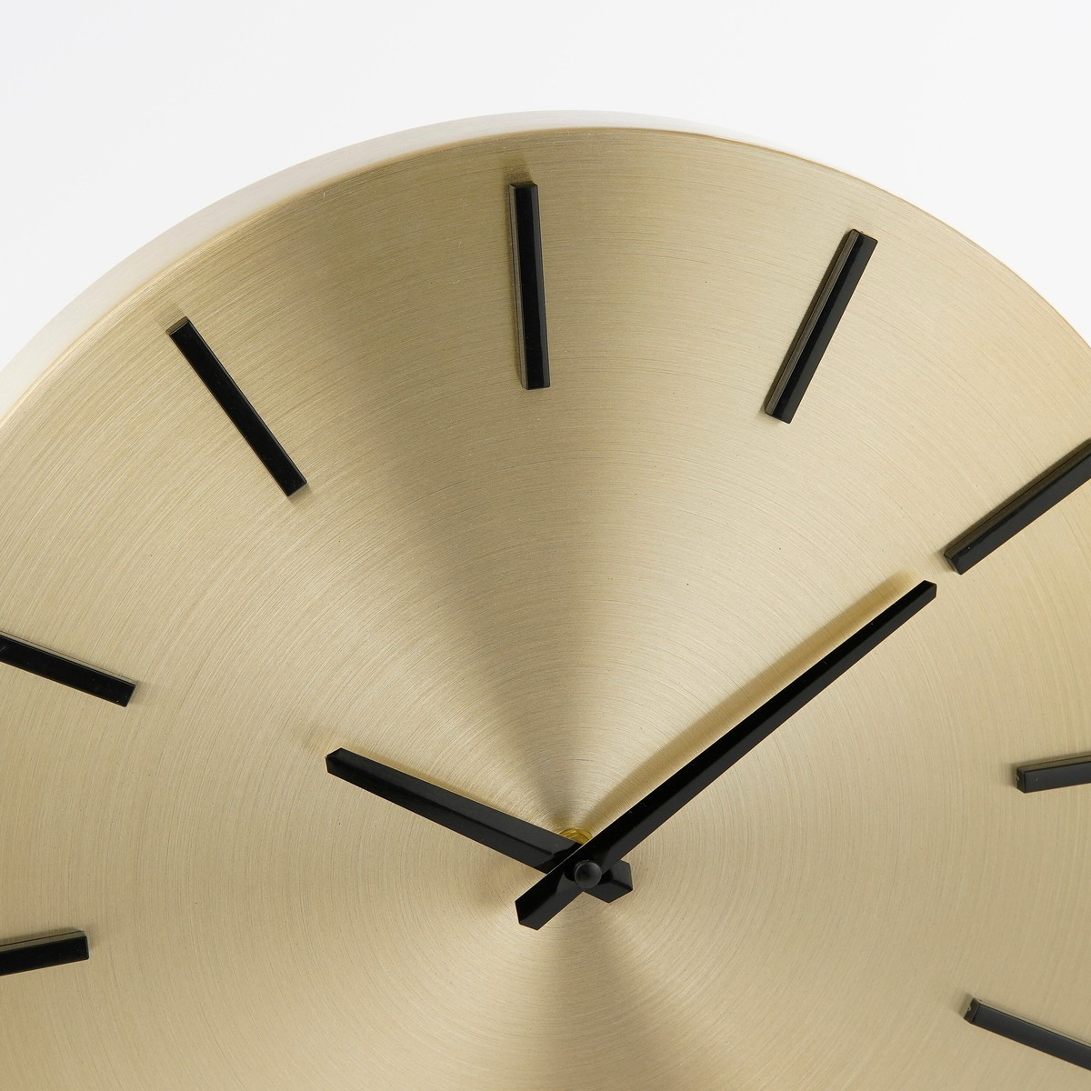 Eine runde, goldfarbene Metallwanduhr mit minimalistischen schwarzen Zeigern und Indizes vor weißem Hintergrund.