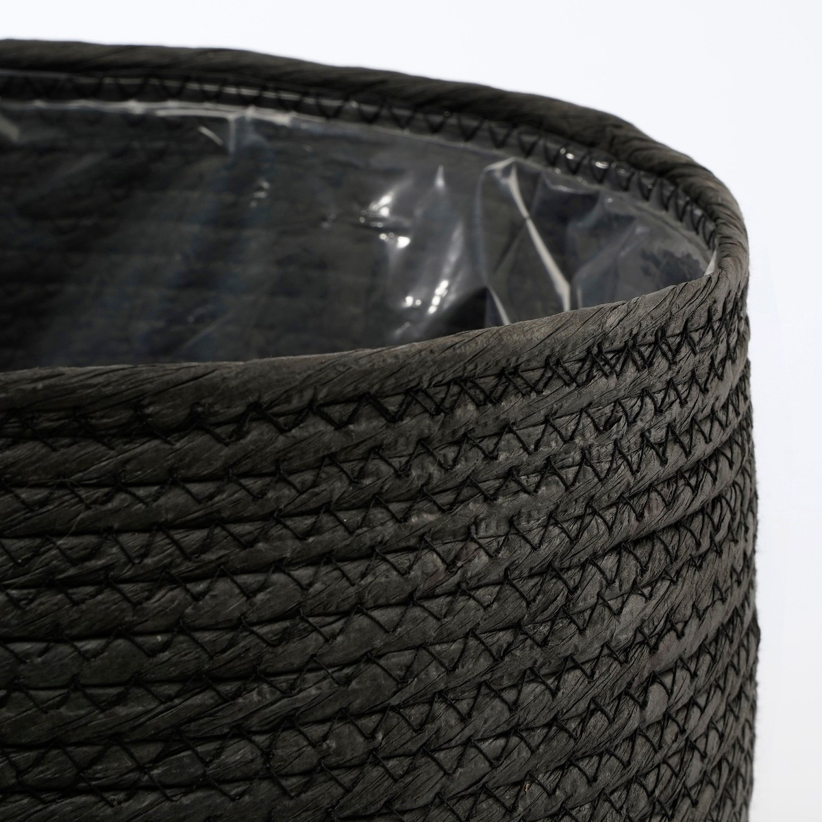 Un panier tressé noir avec une doublure en plastique sur fond blanc.