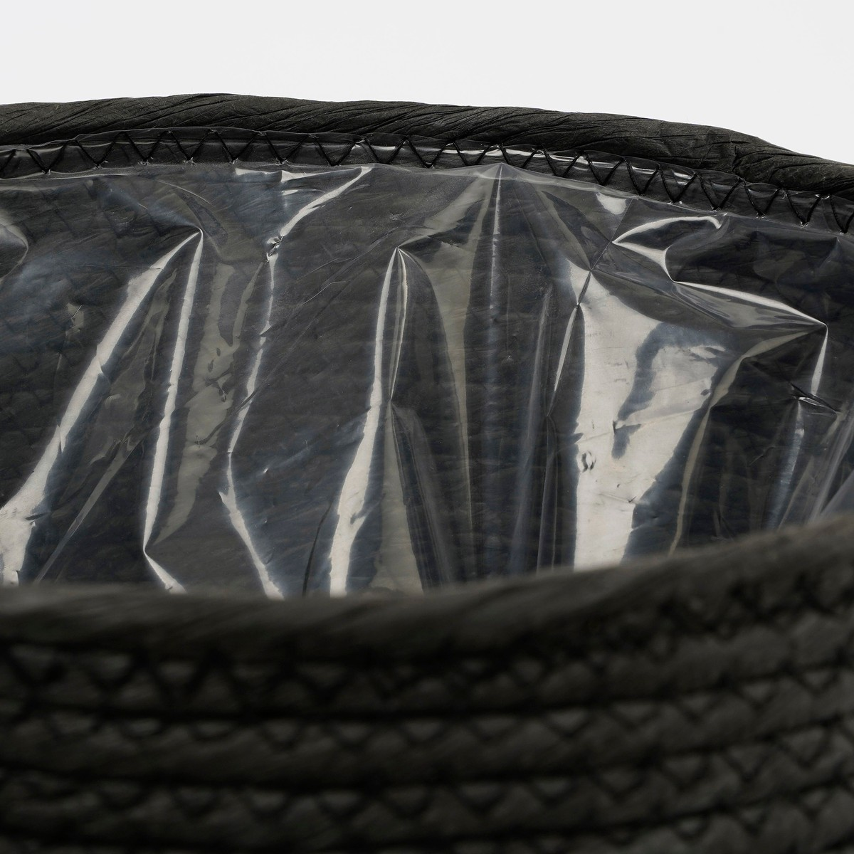 Un panier tissé noir avec une doublure en plastique transparent brillant à l'intérieur, sur fond blanc.