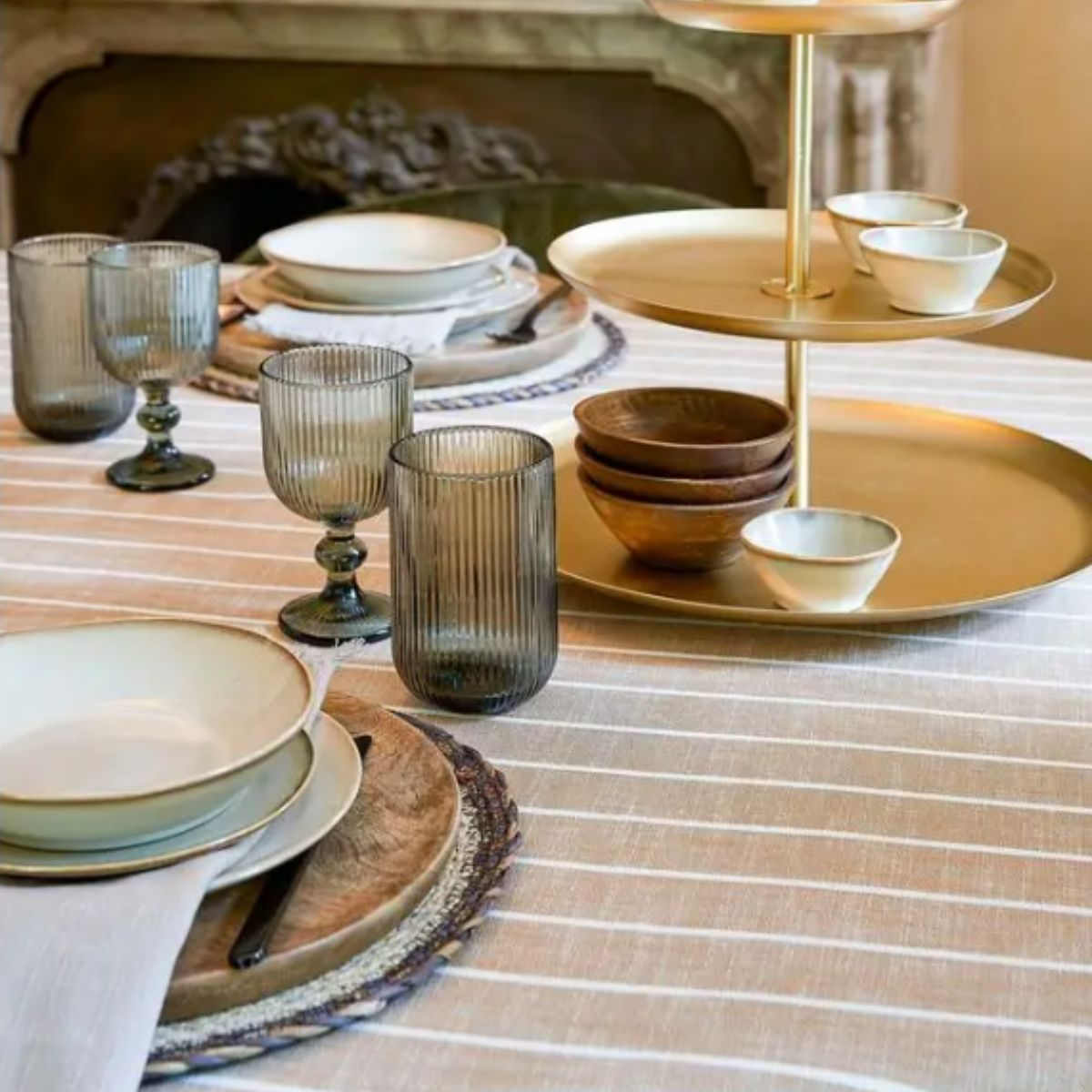 Ein Tisch mit gestreifter Tischdecke, Gläsern, Geschirr und einem goldenen Etagerenhalter.