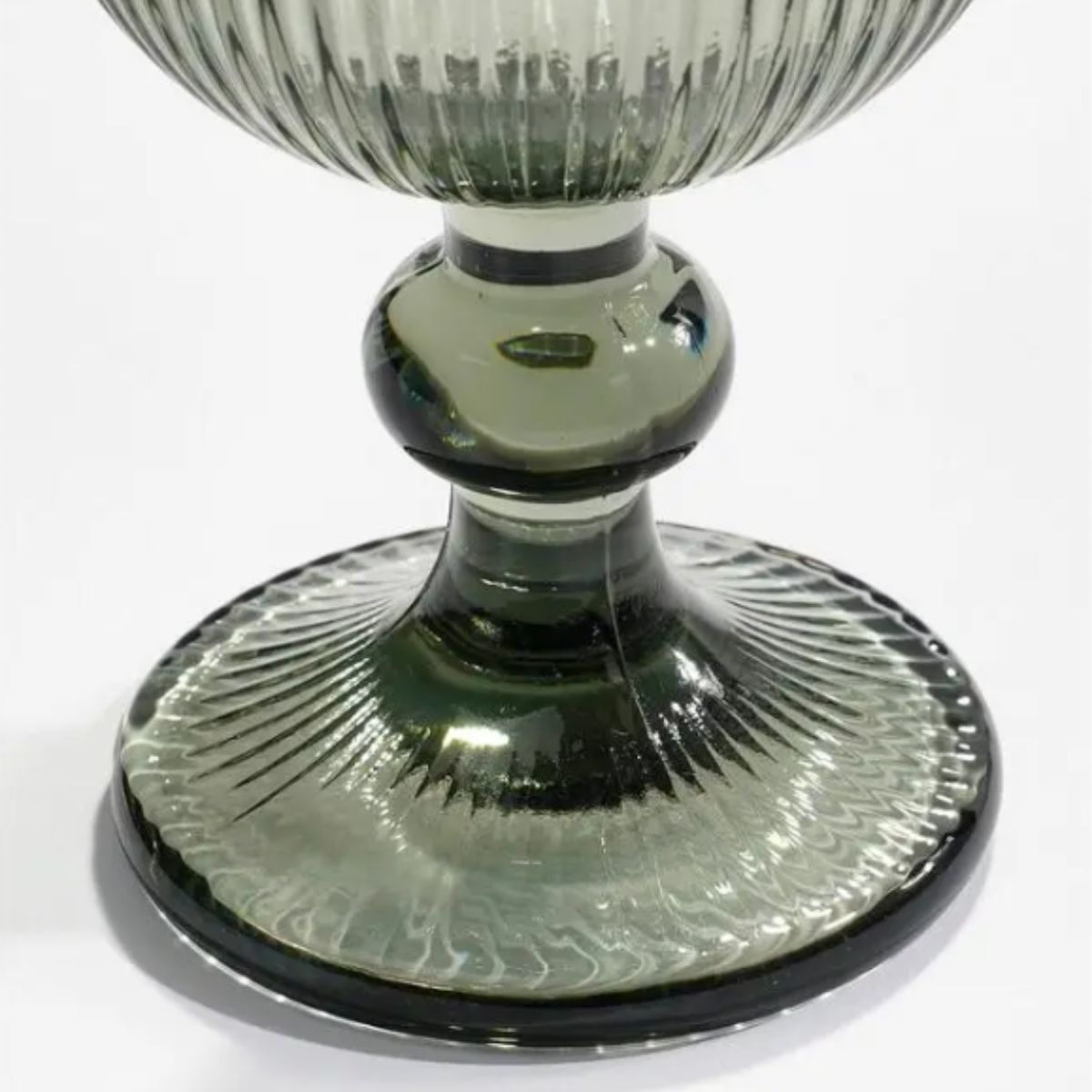 Ein dekorativer Kelch aus grünem Glas mit Rillen und Kugeldetails auf einem flachen Sockel vor weißem Hintergrund.
