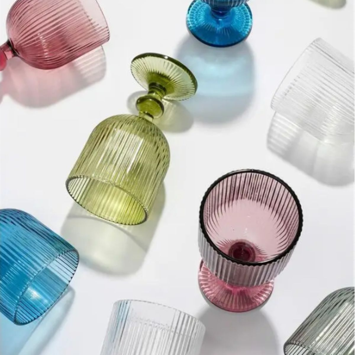 Bunte, gerippte Glaspokale und Becher auf weißem Hintergrund.