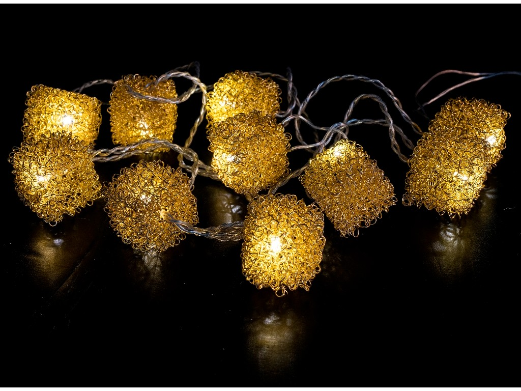 Una cadena de luces con esferas y cubos de malla metálica de color dorado brillante sobre fondo negro.