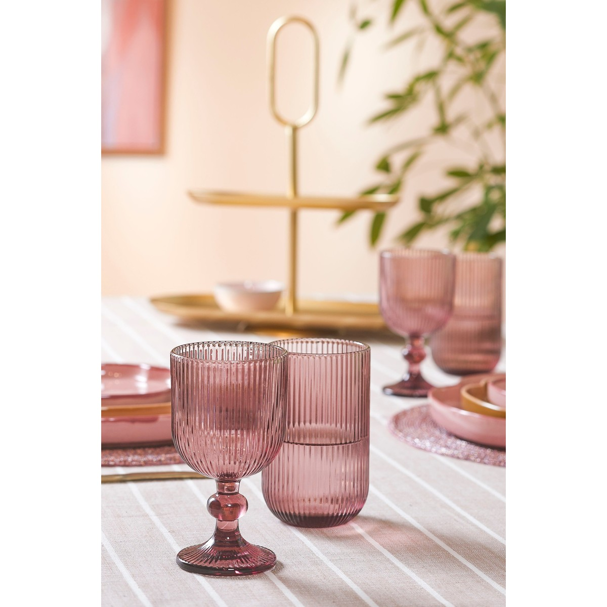 Rosa gerippte Gläser und Teller auf einem Tisch mit goldener Etagere im Hintergrund.