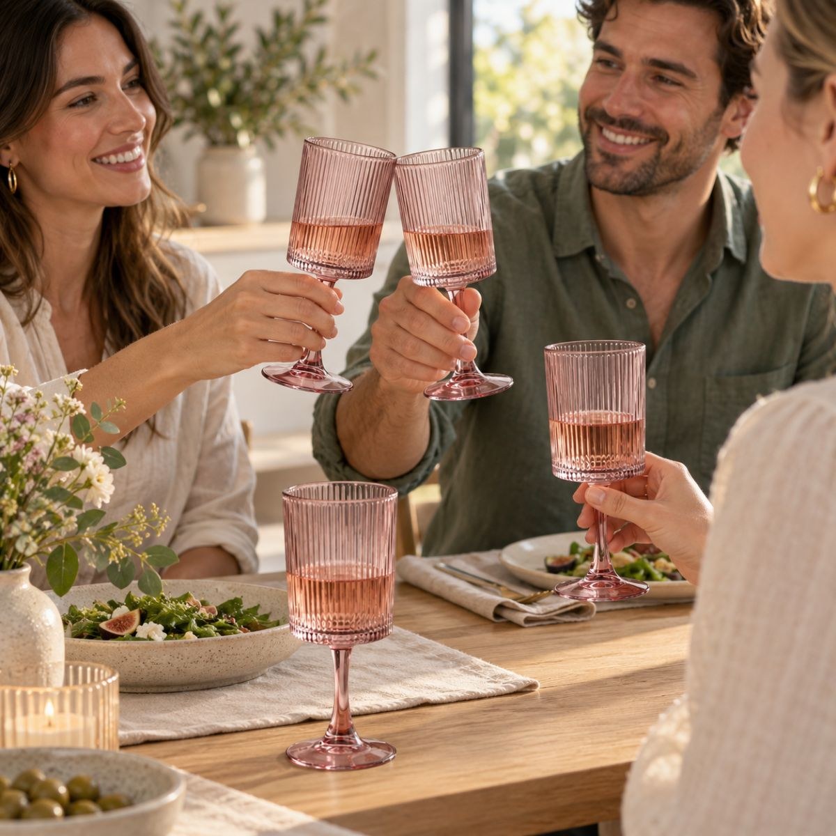 Freunde stoßen mit rosa Gläsern bei einem hellen Essen an.