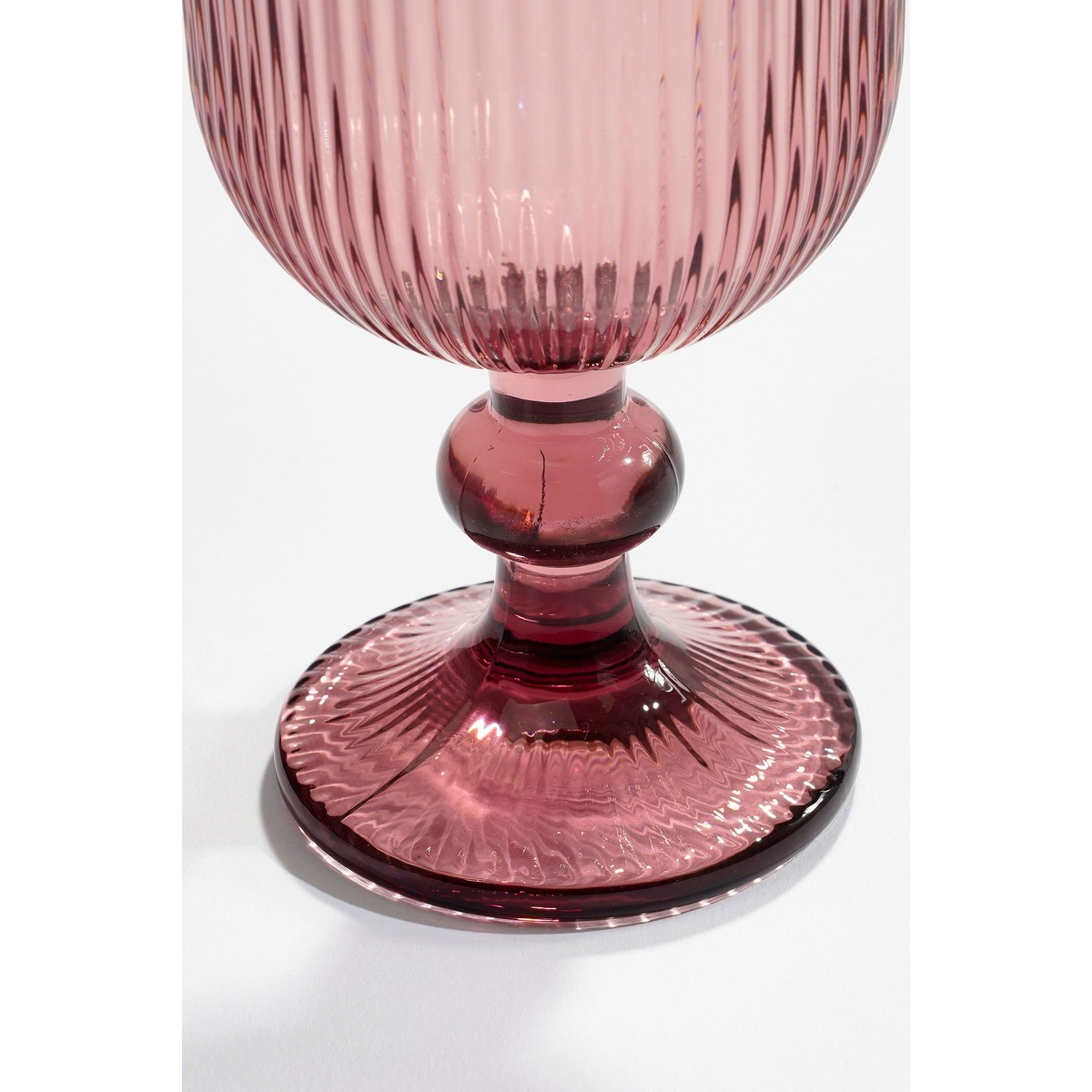 Ein rosa gerippter Kelch steht auf weißer Oberfläche, mit Fokus auf Stiel und Fuß.