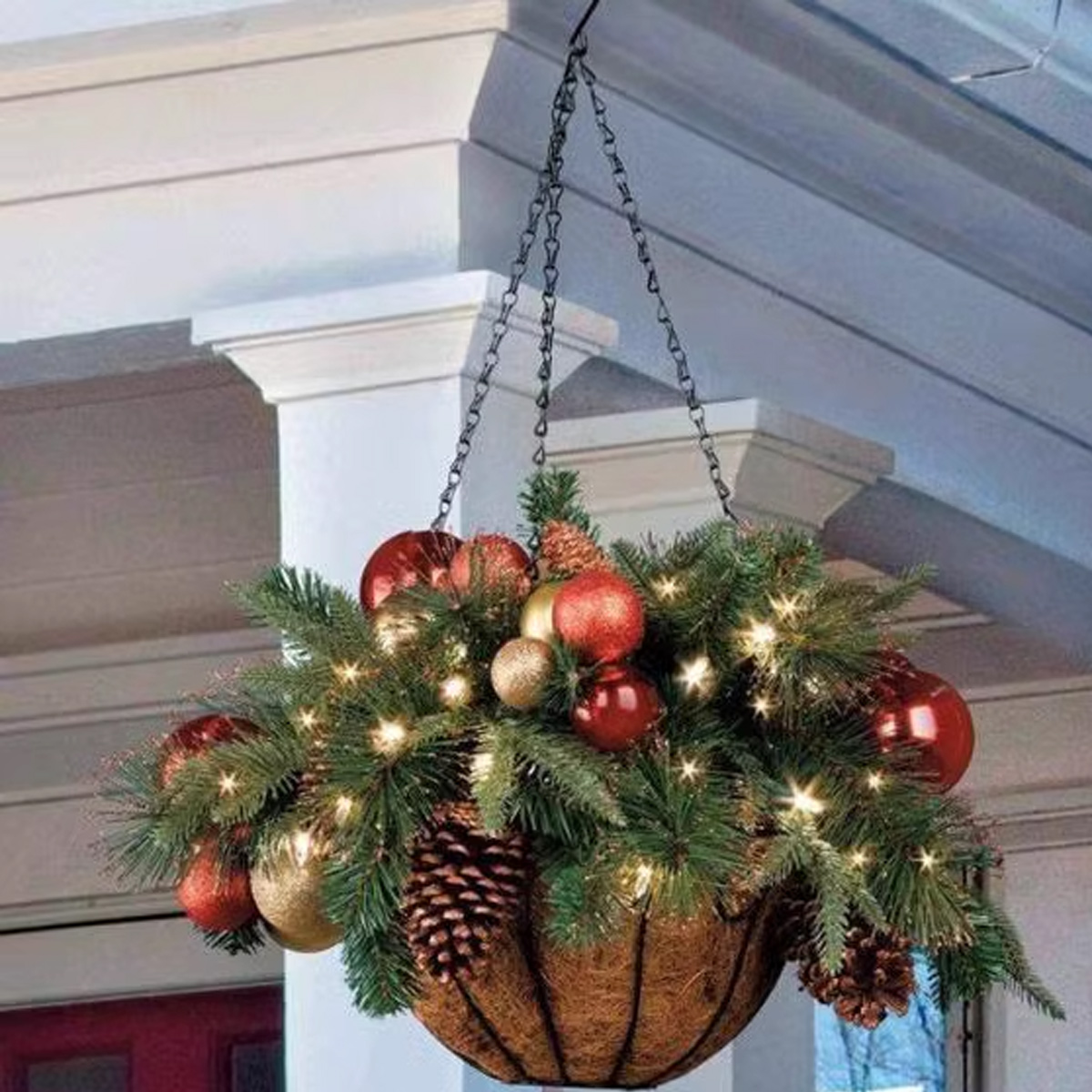 Ein hängender Korb mit grünen Tannenzweigen, roten und goldenen Kugeln, Zapfen und Lichterketten.