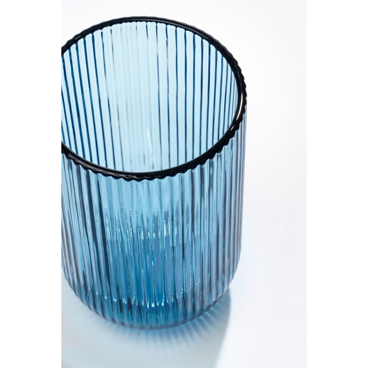 Ein hohes, leeres bluses Trinkglas mit senkrechten Rillen steht auf einer weißen Oberfläche.