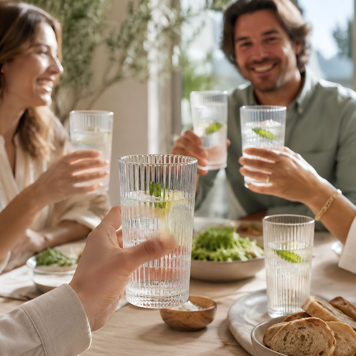 Freunde stoßen an einem gedeckten Tisch mit strukturierten Gläsern voll Wasser und Zitronen an.