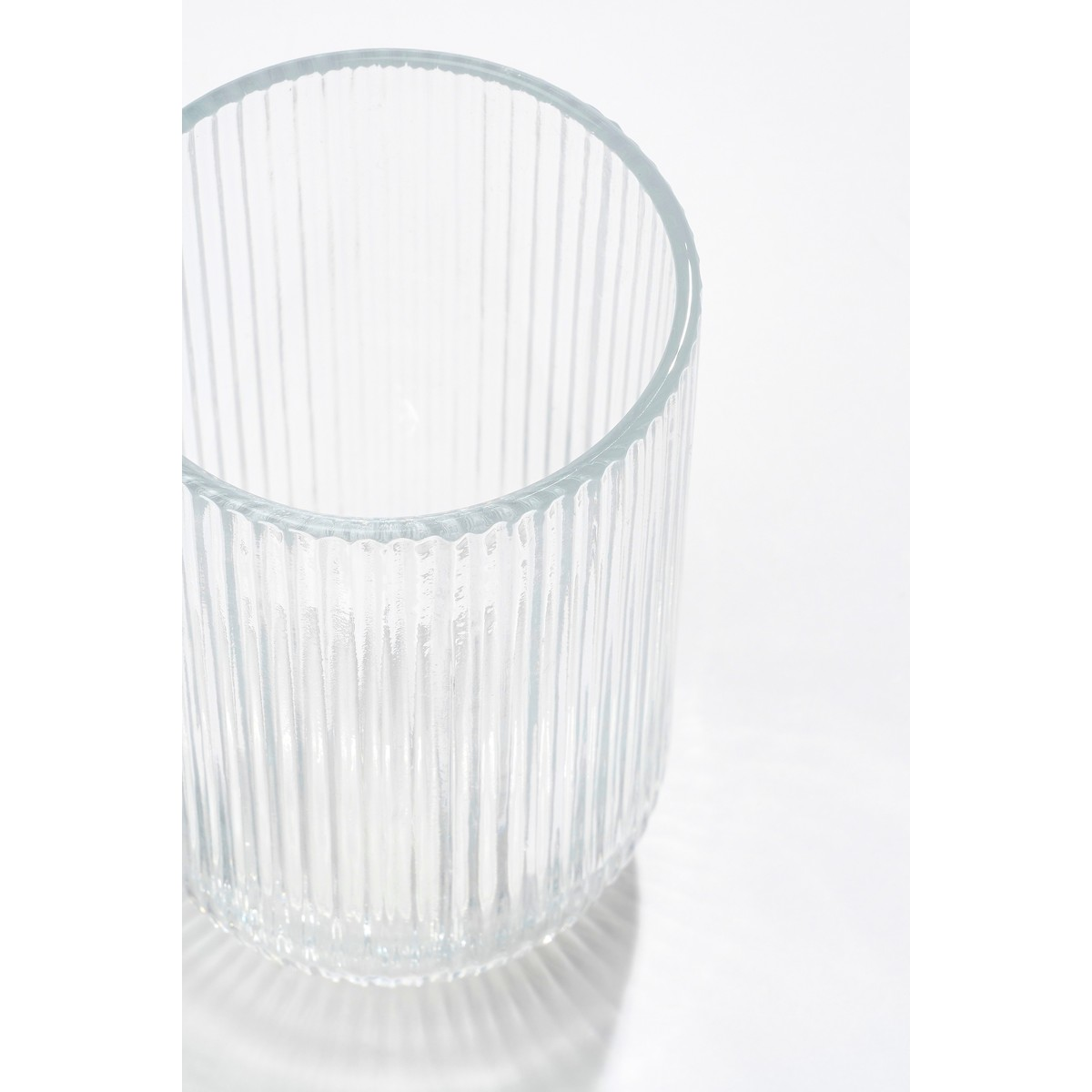 Ein klares, geripptes Glas steht auf einer weißen Oberfläche mit sanftem Schatten.