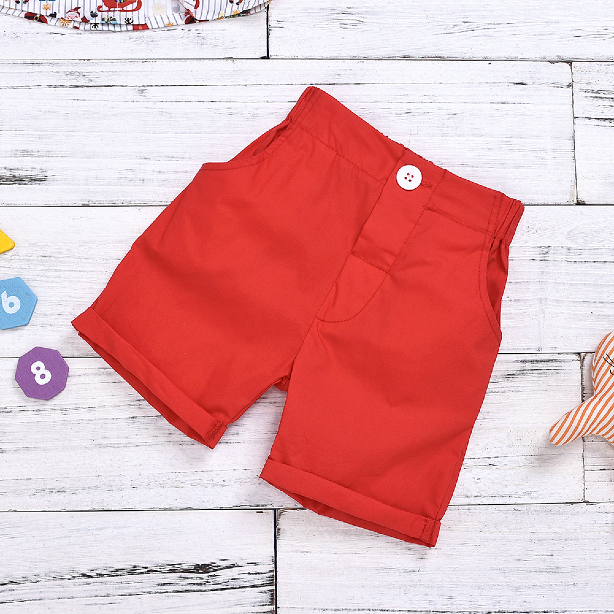 Rote Shorts mit weißem Knopf auf weißem Holzgrund mit bunten Bausteinen.