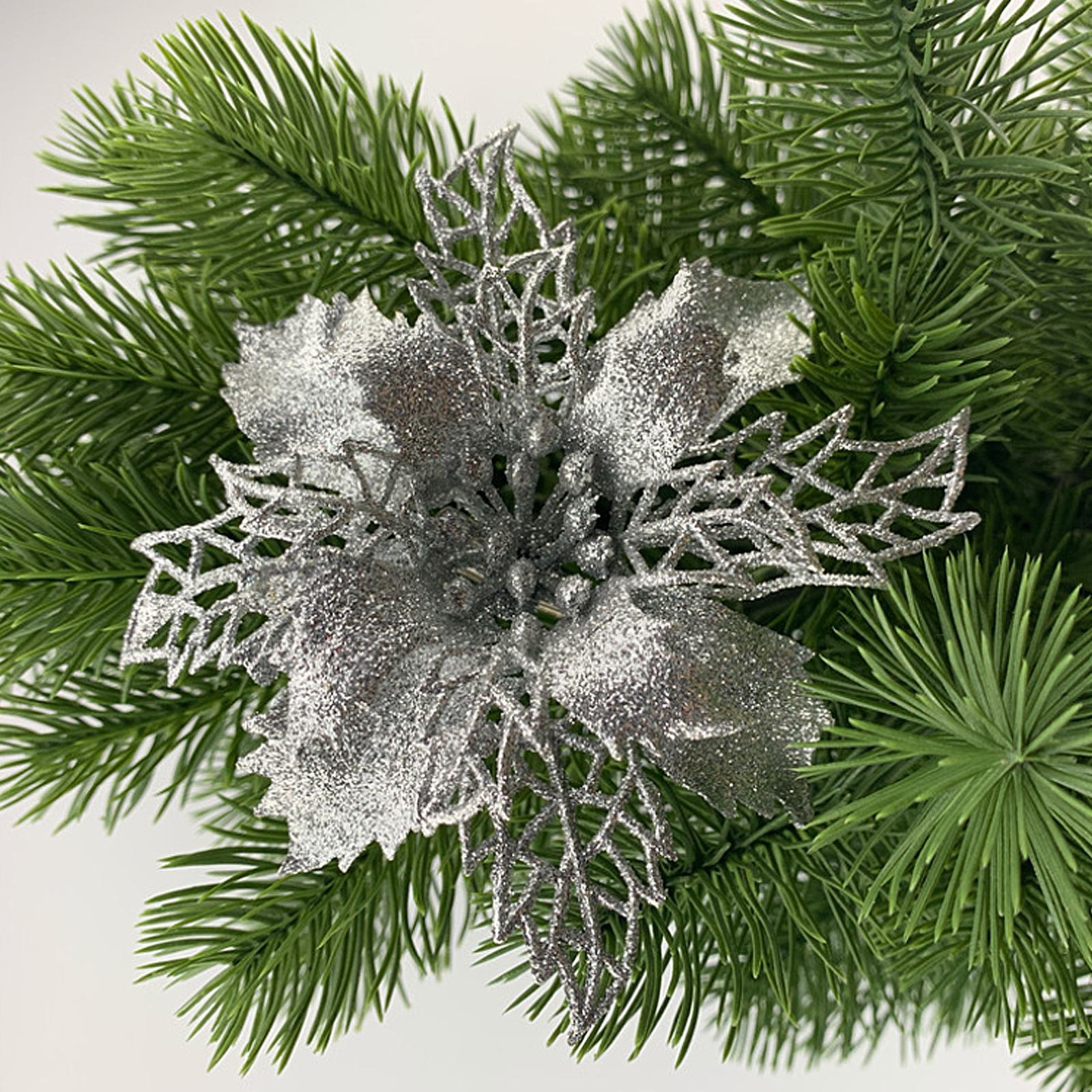 Eine glitzernde silberne Weihnachtsstern-Dekoration liegt auf grünen Tannenzweigen.