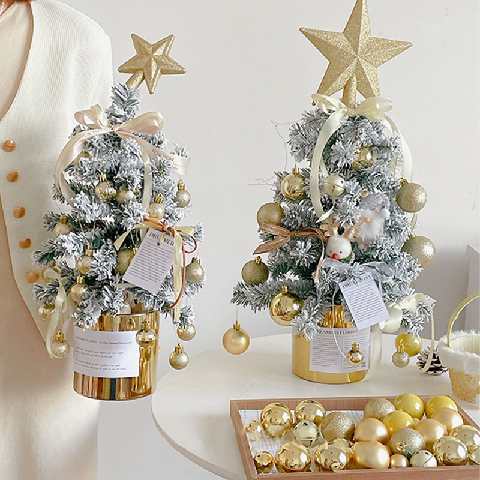 Zwei geschmückte Mini-Weihnachtsbäume in Goldtöpfen mit Kugeln, Schleifen und Sternen.