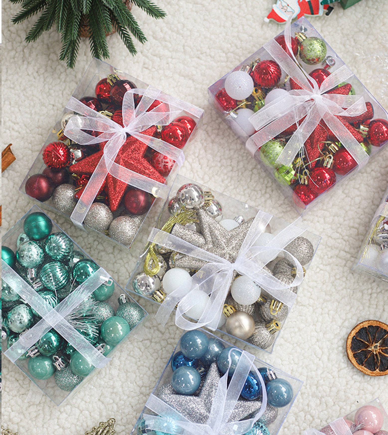 Vier transparente Boxen voller verschiedenfarbiger Weihnachtskugeln und Sterne auf weißem Untergrund.