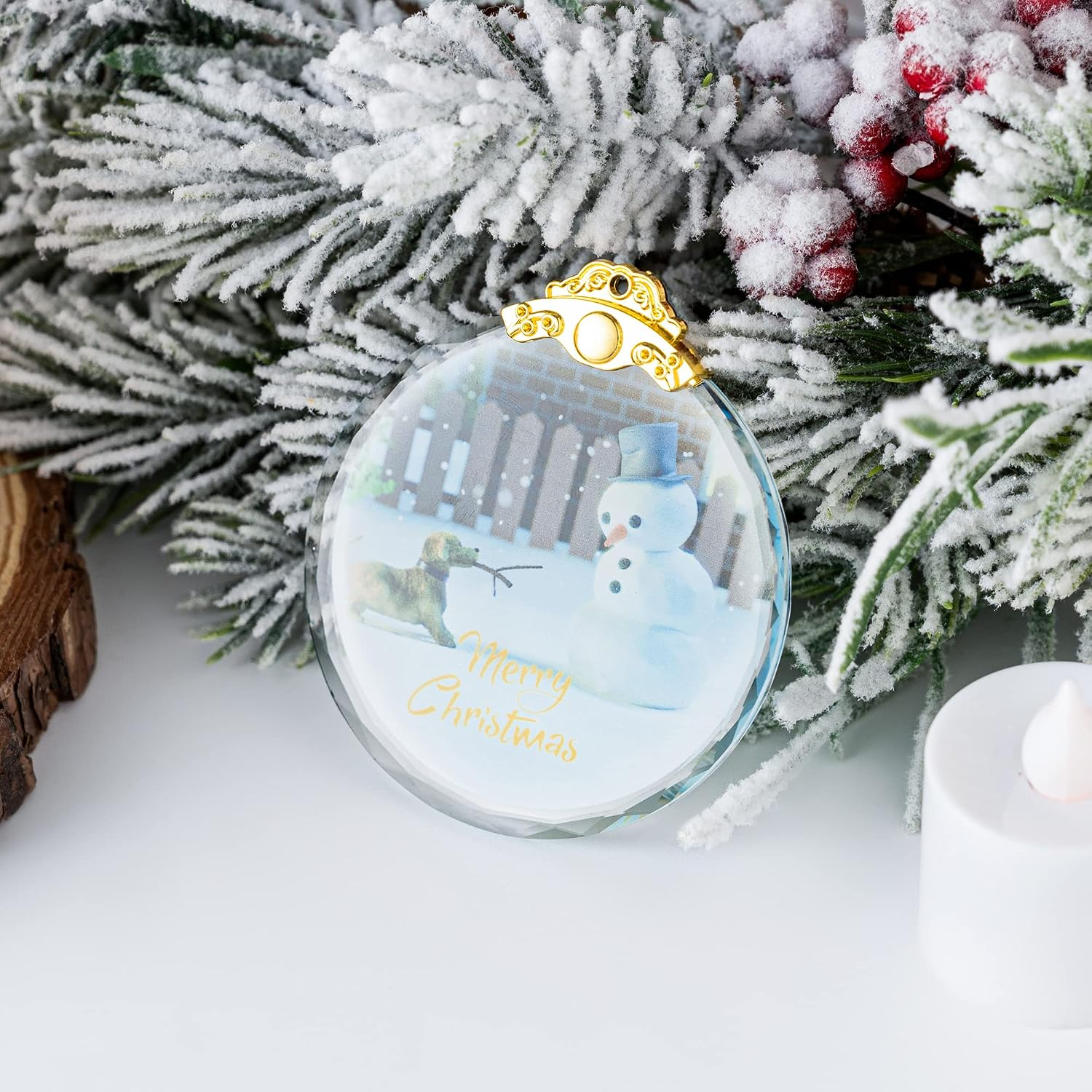 Eine Weihnachtskugel aus Glas mit Schneemann und Hund, umgeben von verschneiten Tannenzweigen und roten Beeren.