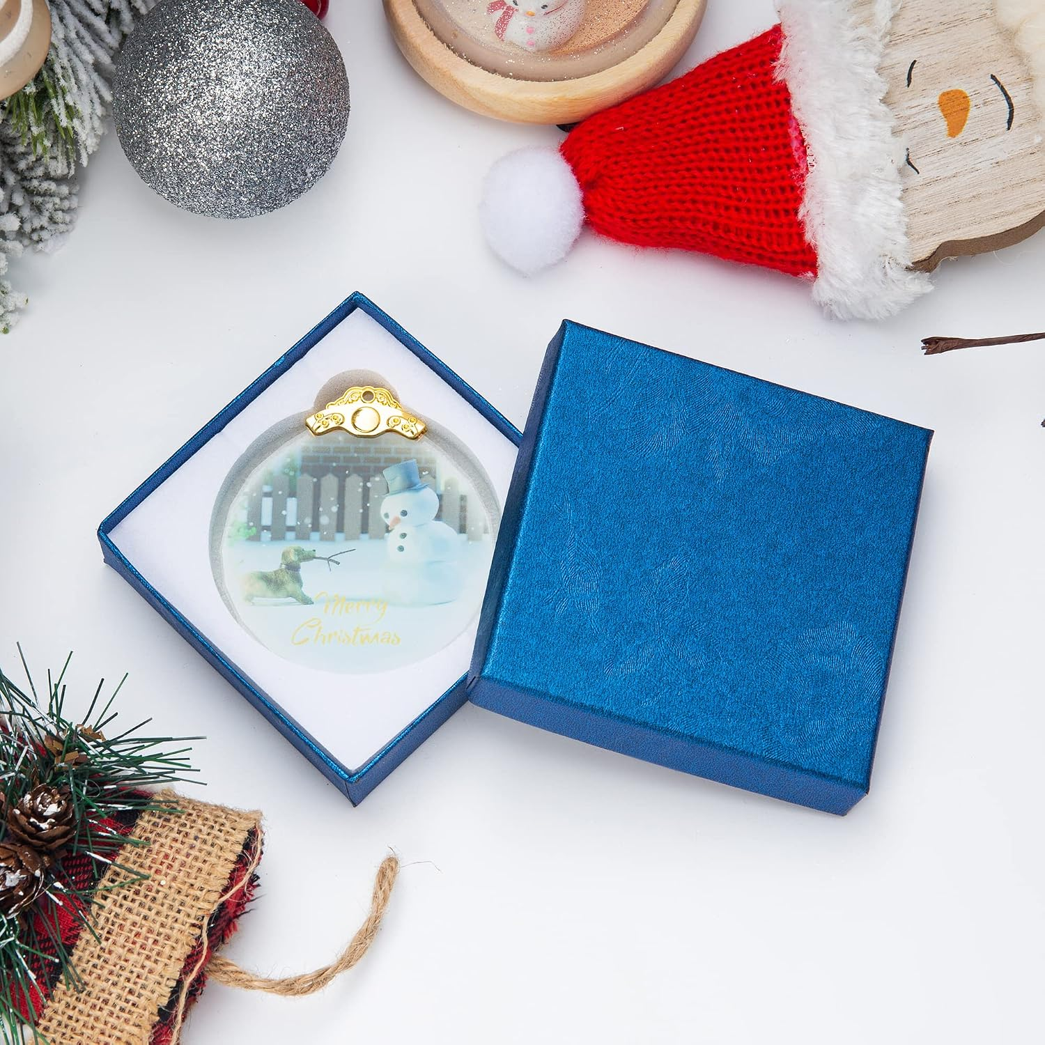 Eine Weihnachtskugel mit Schneemann im blauen Geschenkkasten, umgeben von Deko.