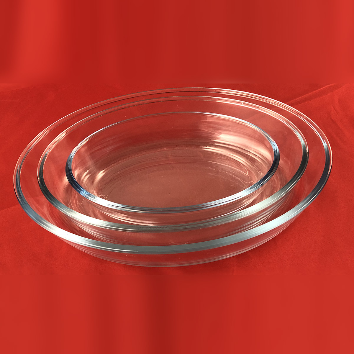 Tres fuentes para horno de vidrio transparente y ovaladas apiladas sobre una superficie roja.