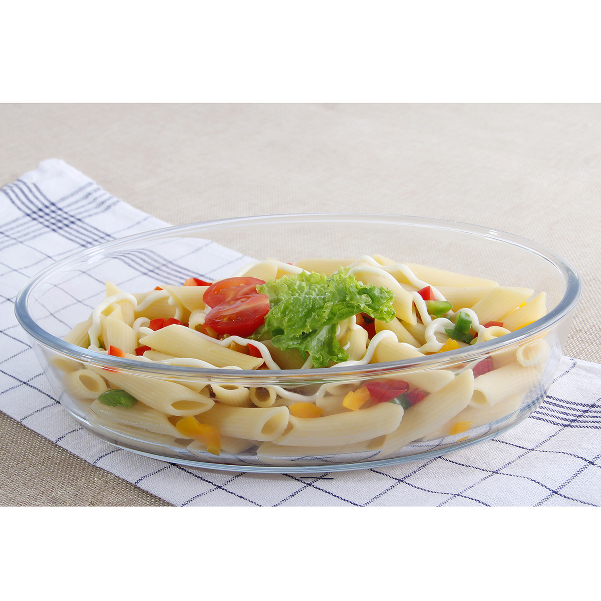 Ensalada de pasta penne con verduras, lechuga y mayonesa en un bol de cristal sobre un paño de cuadros.
