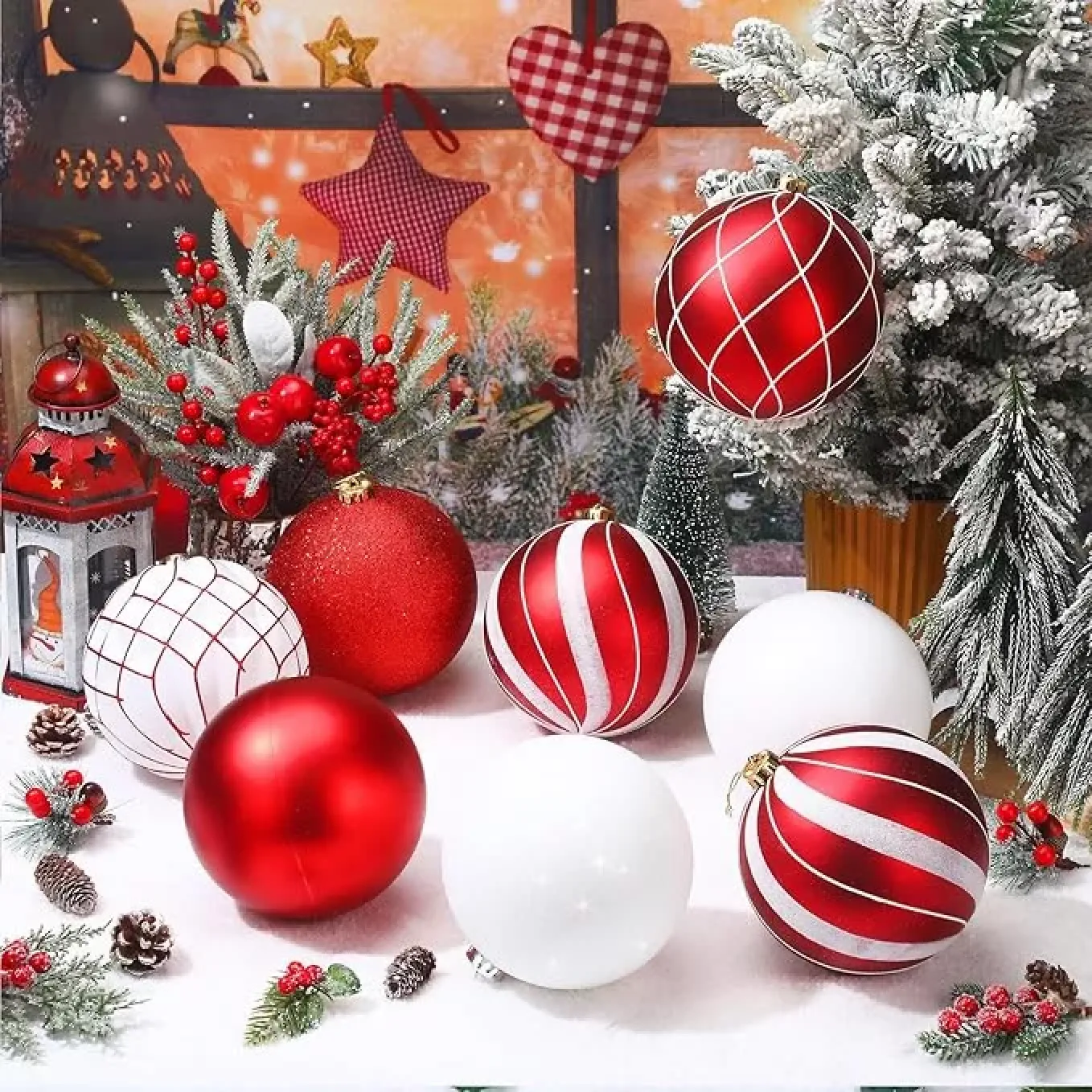 Rote und weiße Weihnachtskugeln liegen im Schnee vor geschmückten Bäumen.