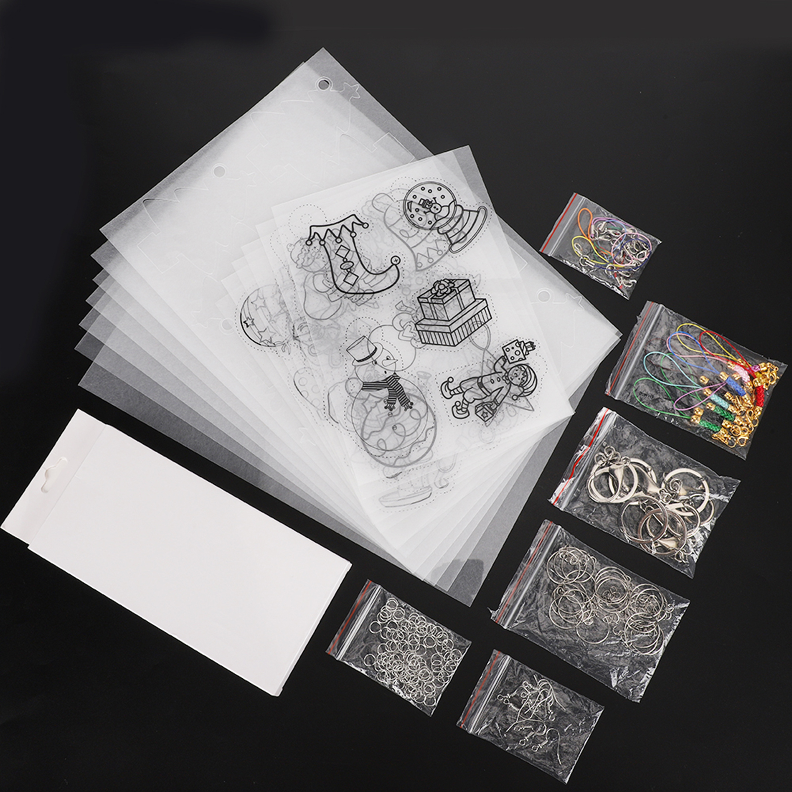 Stapel transparenter Folien mit Weihnachtsmotiven, Zubehörbeutel und weisse Verpackung auf schwarzem Grund.