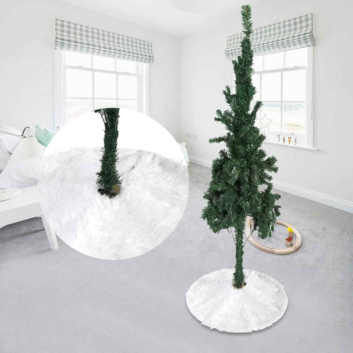 Ein schlanker, künstlicher Weihnachtsbaum in einem hellen Zimmer mit weißem Teppich und weißem Röckchen.