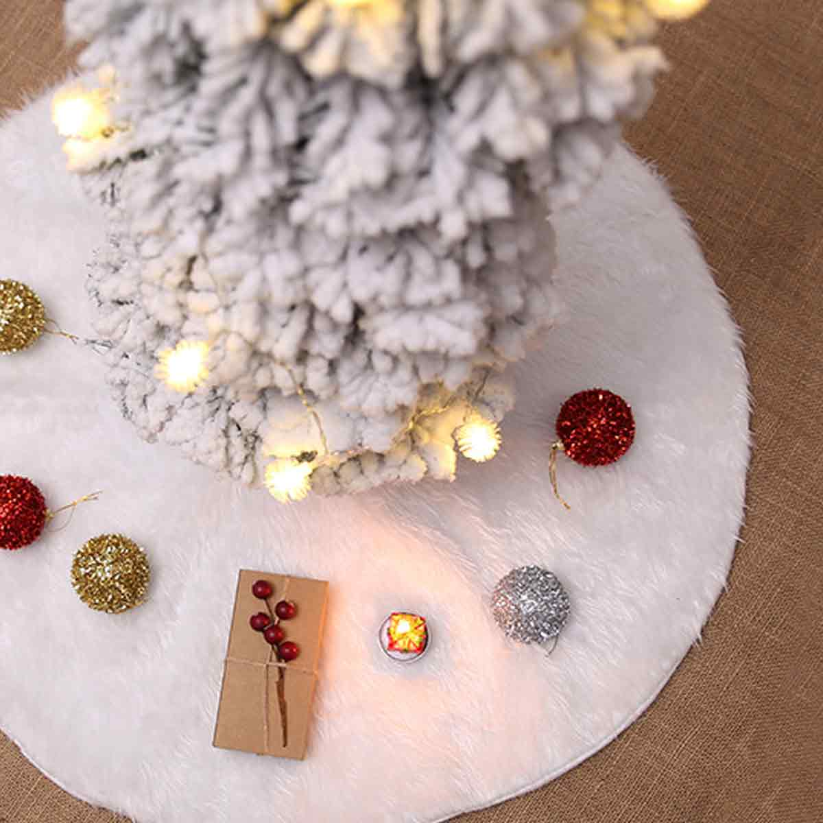 Flockiger Weihnachtsbaum auf weißem Pelzrock mit roten und goldenen Kugeln und einer roten Beeren-Geschenkbox.