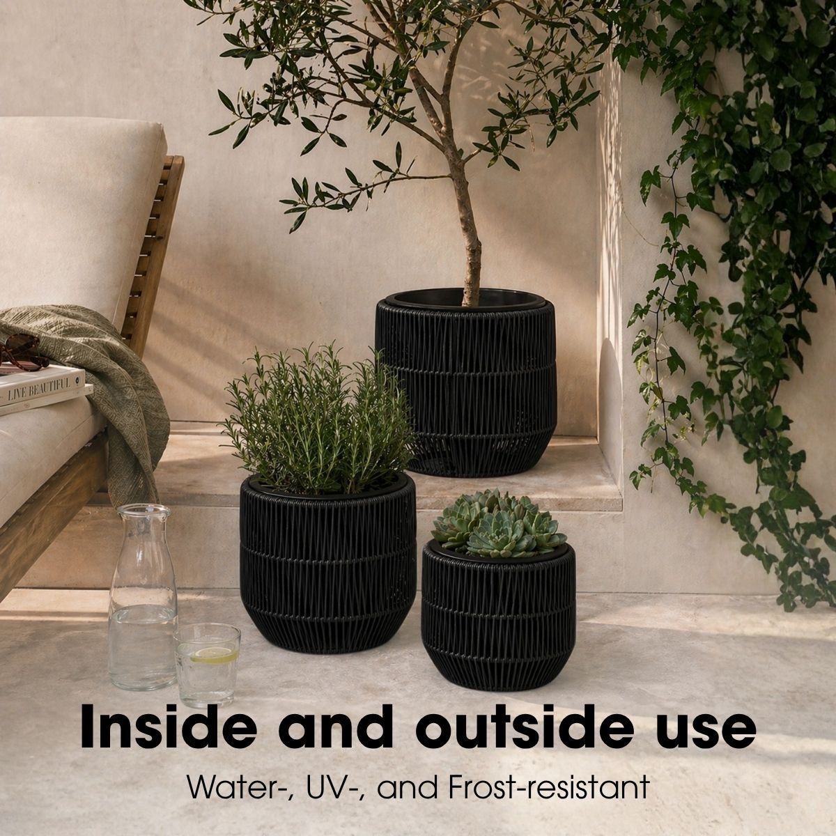 Trois pots de fleurs noirs tressés sur une terrasse avec transat, plantes et lierre.