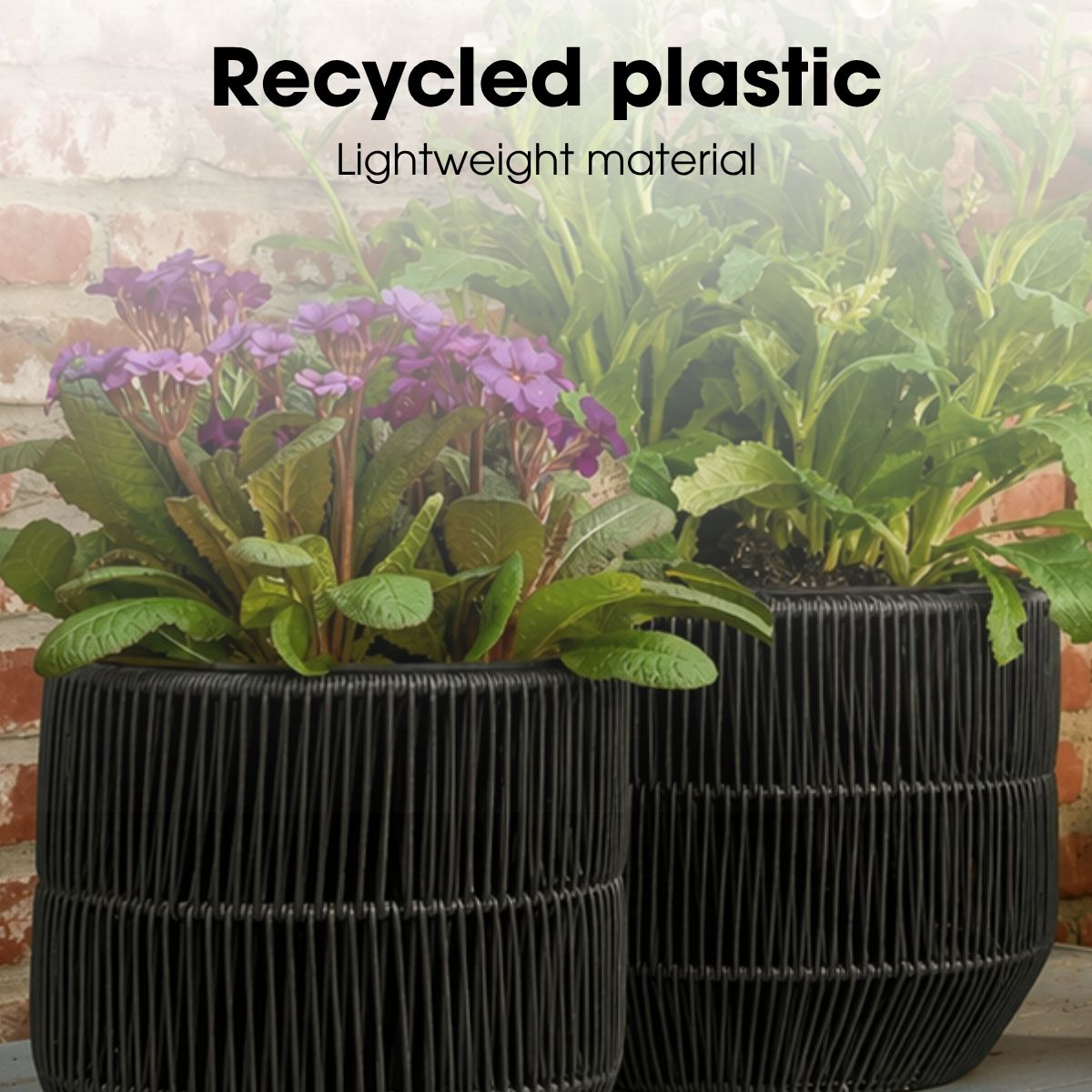 Deux pots de fleurs noirs tissés avec des fleurs violettes et vertes contre un mur de briques, étiquetés Recycled plastic.